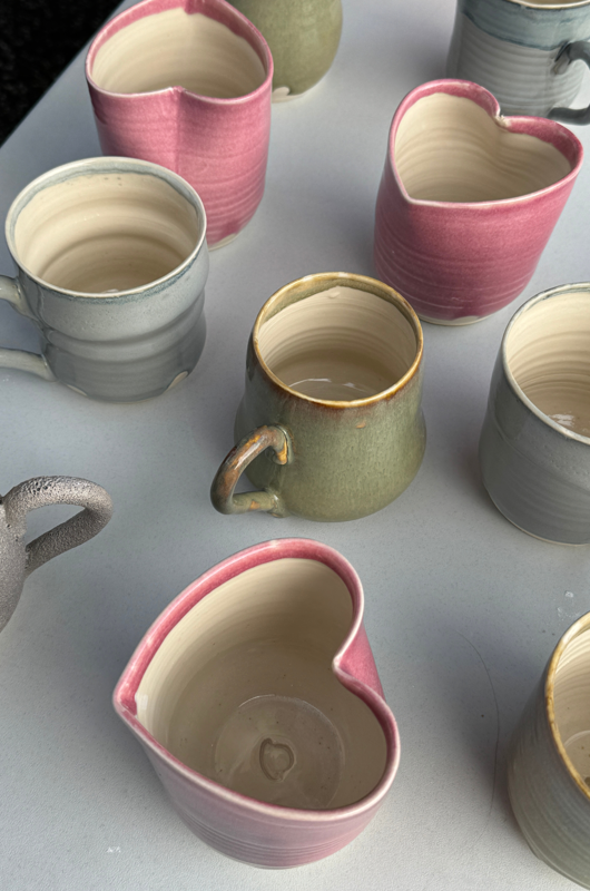 Billede af keramik krus og kopper på et bord, hvor flere af krusene er formet som et hjerte